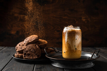 Wall Mural - A glass of iced coffee with milk and chocolate cookies on a plate, cocoa powder falling