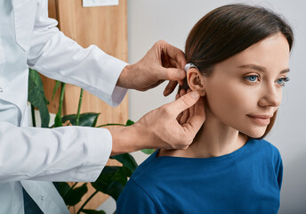 Installation hearing aid on woman's ear at hearing clinic, close-up, side view. Deafness treatment, hearing solutions