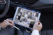 Man holding digital tablet with multiple camera views of office locations while sitting in car. Freelance, business trip, modern technology concept