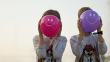 Children Cover Their Faces With Bright Inflatable Balloons With Drawings Of Smiles On Them