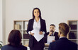 © Studio Romantic - Portrait of female lawyer or attorney who represents plaintiff in lawsuit during court trial. Serious unsmiling woman holding documents standing in courtroom after her speech in front of audience