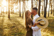 Embracing And Kissing. Happy Couple Is Outdoors In The Forest At Daytime