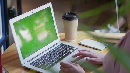 Over the shoulder shot of a business woman working in office interior on pc on desk, looking at green screen. Office person using laptop computer with laptop green screen, sitting at wooden table