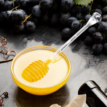 Honey In Glass Jar With Honey Spoon On Dark Stone Board With Wine Cheese Corkscrew In Black Juicy Grapes Frame. Delicious Yellow Bee Honey In Snack Plate On Black Table. Square Photo