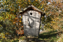 Old Countryside Wood Toilet In Autumn Conditions With Yellow And Orange Leaves. Decorative Heart Engraving On The Doors.