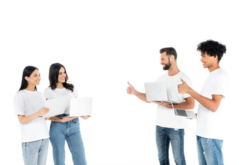 Poster - cheerful interracial freelancers showing thumbs up to women with laptops isolated on white.