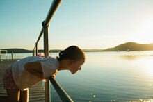 Young Girl At A Wharf Leaning Over Looking At The Water