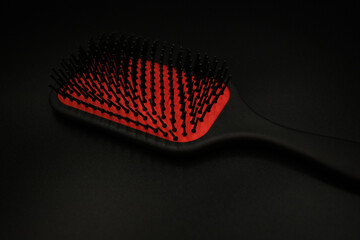 on a black background lies a wide massage comb of black and red color