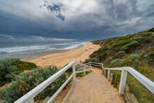 Looking Down A Fenced Staircase To A Sandy Beach Below And Dark Stormy Clouds Overhead