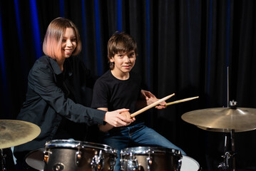 Young woman teaching boy to play drums.