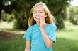 © Roquillo - Caucasian little kid girl wearing blue T-shirt standing outdoors touching mouth with hand with painful expression because of toothache or dental illness on teeth.