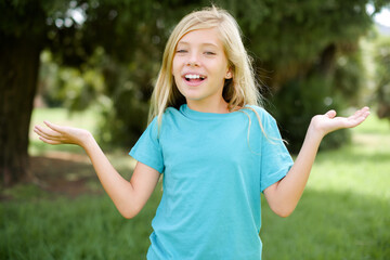 Wall Mural - Caucasian little kid girl wearing blue T-shirt standing outdoors celebrating crazy and amazed for success with arms raised and open eyes screaming excited. Winner concept