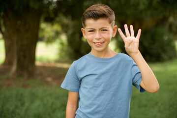 Wall Mural - beautiful Caucasian little kid boy wearing blue T-shirt standing outdoors showing and pointing up with fingers number four while smiling confident and happy.