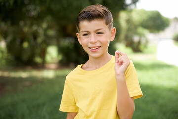 Wall Mural - Caucasian little kid boy wearing yellow T-shirt standing outdoors pointing up with hand showing up seven fingers gesture in Chinese sign language QÄ«.