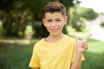 Wall Mural - Caucasian little kid boy wearing yellow T-shirt standing outdoors pointing up with fingers number eight in Chinese sign language BÄ.