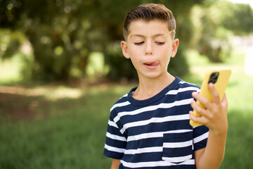 Photo of nice pretty beautiful Caucasian little kid boy wearing stripped T-shirt standing outdoors demonstrate phone screen hold hair tails