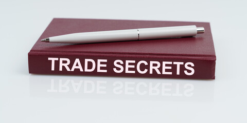 Poster - On a white surface lies a pen and a notebook with the inscription - TRADE SECRETS