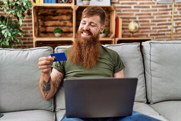 Canvas Print - Young redhead man using laptop and credit card at home