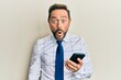 © Krakenimages.com - Middle age businessman using smartphone scared and amazed with open mouth for surprise, disbelief face