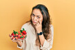 Young hispanic girl holding strawberries pointing to the eye watching you gesture, suspicious expression