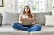 © Krakenimages.com - Beautiful young brunette woman sitting on the sofa using computer laptop at home puffing cheeks with funny face. mouth inflated with air, crazy expression.