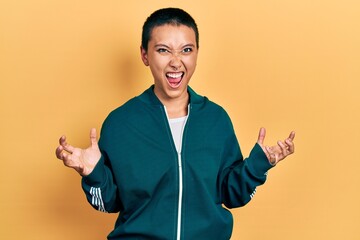 Wall Mural - Beautiful hispanic woman with short hair wearing sporty jacket crazy and mad shouting and yelling with aggressive expression and arms raised. frustration concept.