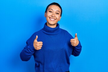 Beautiful hispanic woman with short hair wearing turtleneck sweater success sign doing positive gesture with hand, thumbs up smiling and happy. cheerful expression and winner gesture.