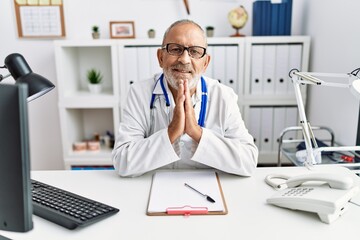 Canvas Print - Mature doctor man at the clinic praying with hands together asking for forgiveness smiling confident.