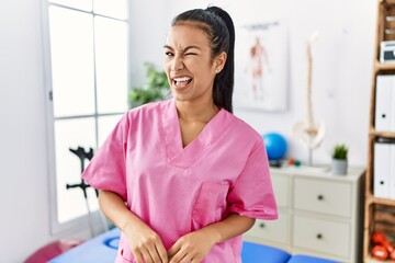 Sticker - Young hispanic woman working at pain recovery clinic winking looking at the camera with sexy expression, cheerful and happy face.