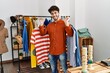 © Krakenimages.com - Young hispanic customer man smiling happy holding clothes at clothing store.