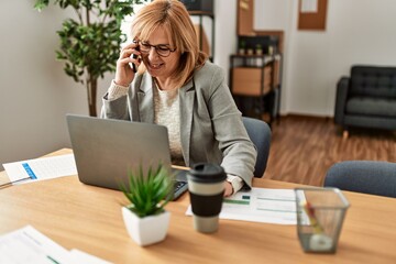 Canvas Print - Middle age businesswoman working using laptop and talking on the smartphone at the office.