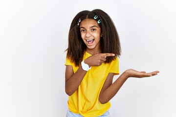 Sticker - Young african american girl standing over white isolated background amazed and smiling to the camera while presenting with hand and pointing with finger.