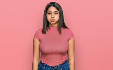 Sticker - Young hispanic girl wearing casual t shirt puffing cheeks with funny face. mouth inflated with air, crazy expression.