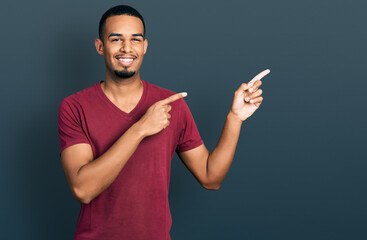 Young african american man wearing casual t shirt smiling and looking at the camera pointing with two hands and fingers to the side.