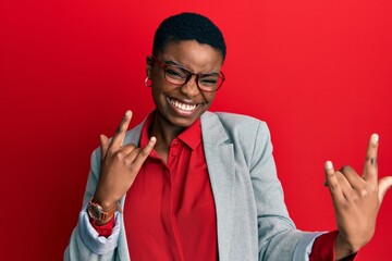 Young african american woman wearing business jacket and glasses shouting with crazy expression doing rock symbol with hands up. music star. heavy concept.