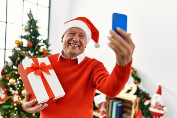 Wall Mural - Senior grey-haired man holding christmas gift making selfie by the smartphone at home.