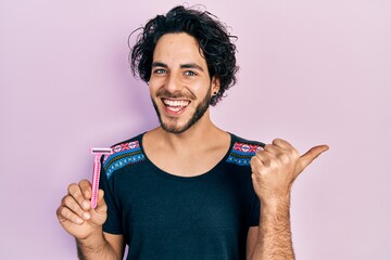 Poster - Handsome hispanic man holding razor pointing thumb up to the side smiling happy with open mouth