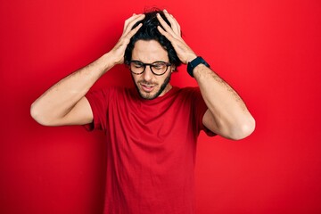 Poster - Handsome hispanic man wearing casual t shirt and glasses suffering from headache desperate and stressed because pain and migraine. hands on head.