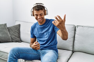 Poster - Young hispanic man relaxing sitting on the sofa wearing headphones at home