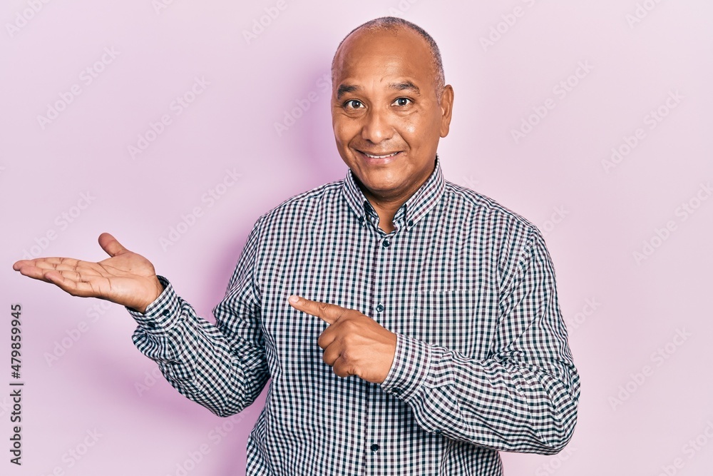 Middle age latin man wearing casual clothes amazed and smiling to the camera while presenting with hand and pointing with finger.