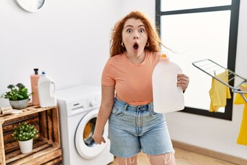 Canvas Print - Young redhead woman doing laundry holding detergent bottle scared and amazed with open mouth for surprise, disbelief face