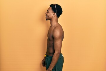 Young african american man wearing swimwear and swimmer glasses looking to side, relax profile pose with natural face and confident smile.