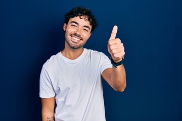 Wall Mural - Young hispanic man wearing casual white t shirt smiling happy and positive, thumb up doing excellent and approval sign