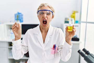 Poster - Middle age blonde woman working at laboratory angry and mad screaming frustrated and furious, shouting with anger. rage and aggressive concept.