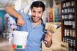© JackF - Satisfied young cheerful positive smiling man standing amongst racks in paint store with brushes and paint