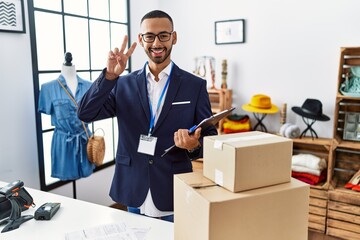 Poster - African american man working as manager at retail boutique smiling looking to the camera showing fingers doing victory sign. number two.