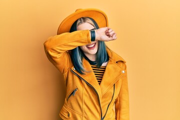 Wall Mural - Young modern girl wearing yellow hat and leather jacket covering eyes with arm smiling cheerful and funny. blind concept.