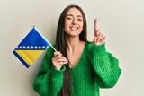 Fototapeta  - Young hispanic girl holding bosnia herzegovina flag smiling with an idea or question pointing finger with happy face, number one