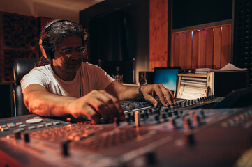 Senior hispanic music producer working on a mixing soundboard while in his studio