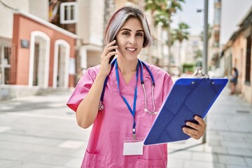 Sticker - Young caucasian doctor woman talking on the smartphone and reading checklist at the city.